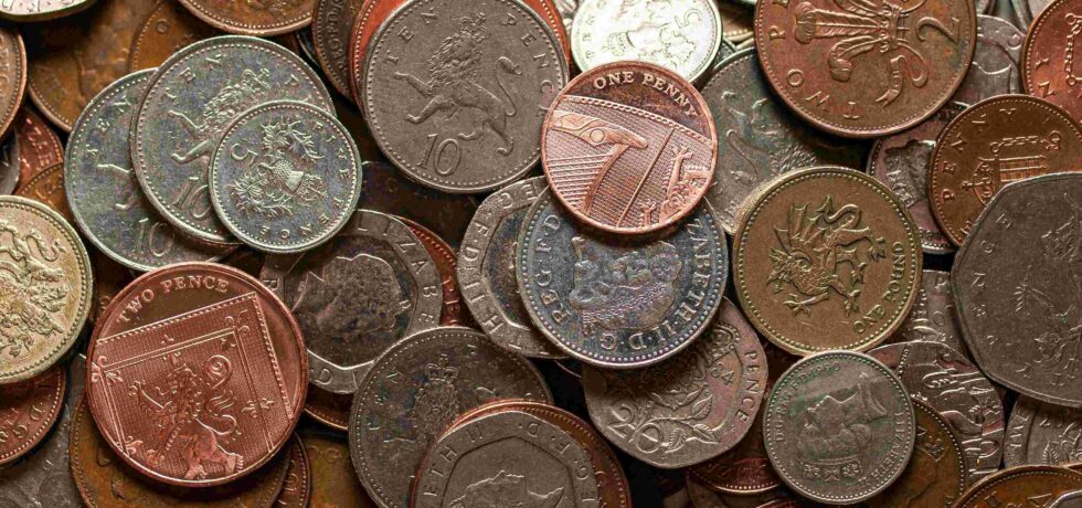 Multiple different UK coins on one another on a table, filling the image