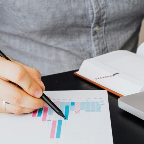 laptop, book and graph on display, person reviewing data on graph with pencil