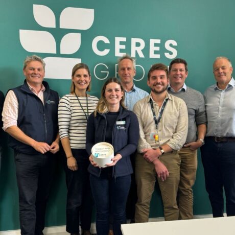 9 people from Ceres Research standing in a row in front of the Ceres Group display wall, one person at the front is holding a small cake that says "happy 1-year anniversary" on the top with the Ceres Research logo.