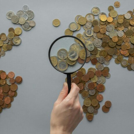 world map on table made out of coins with a hand holding a magnifying glass