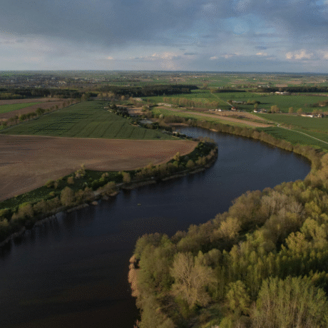 Image of farmland, with a river going through the middle and houses in the distance