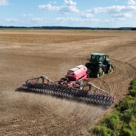 Drone shot of a tractor plowing a vast field, set in a countryside landscape