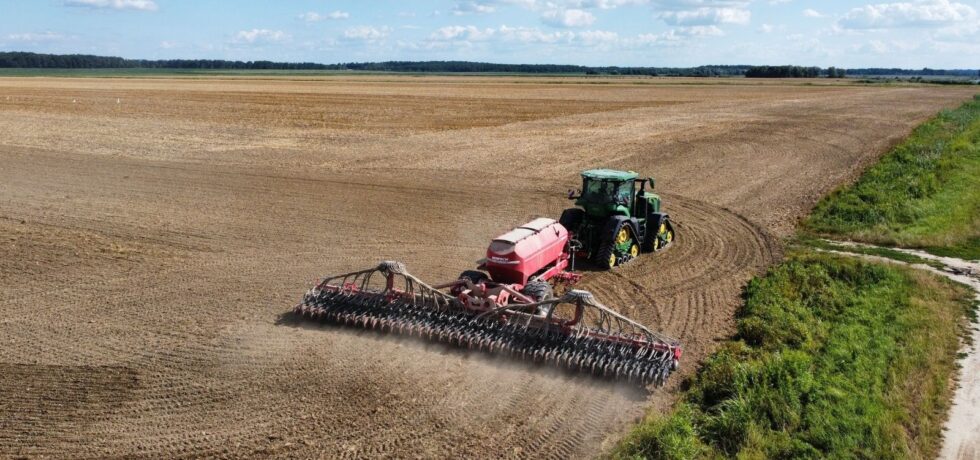 Drone shot of a tractor plowing a vast field, set in a countryside landscape